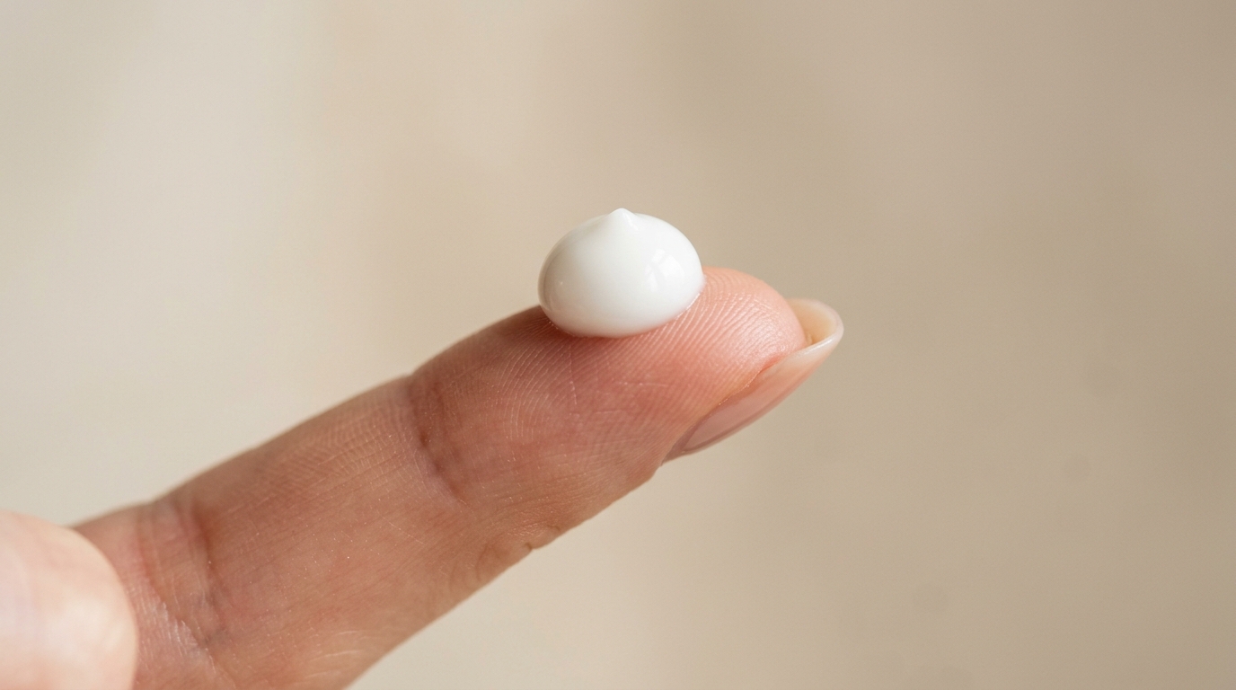 Clean fingertip holding an exact pea-sized amount of white retinol face cream